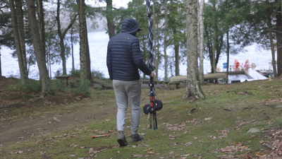 Person walking with fishing rods in a forested area near a lake